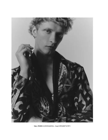 Black and white portrait of a young adult male with blond hair wearing patterned shirt and scarf in front of a plain background.