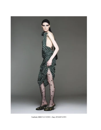 Fashion photo of an adult woman wearing a green and white polka-dot dress, black polka-dot tights, and heeled shoes against a gray background.