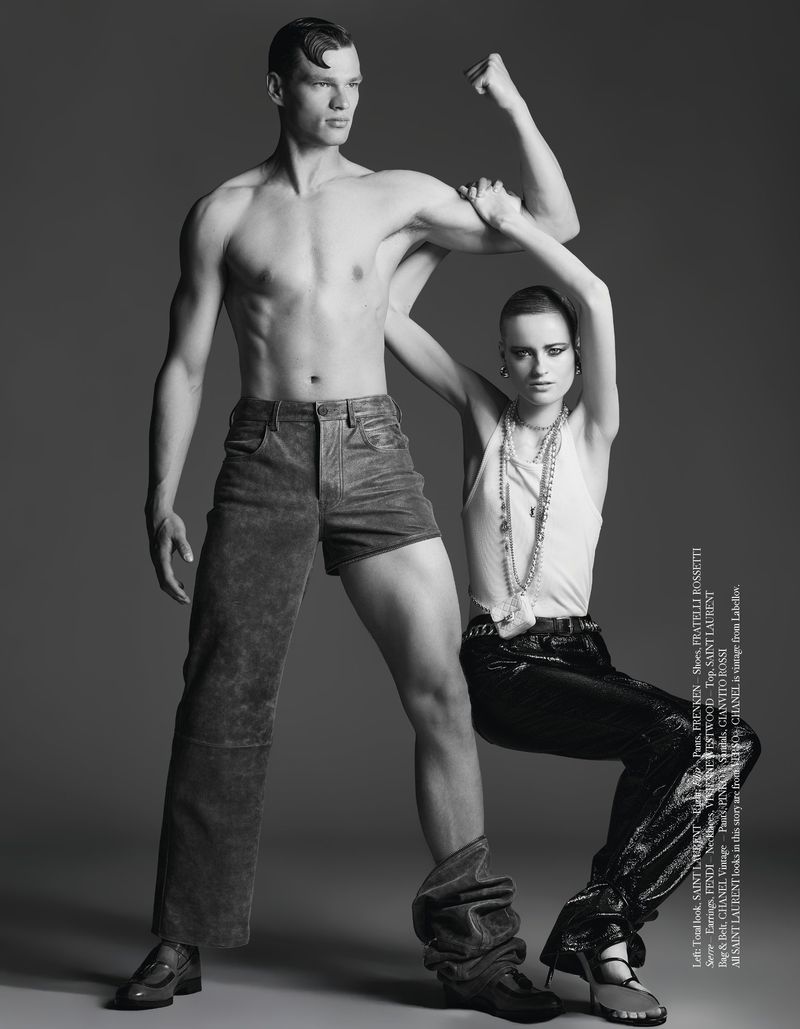 Fashion editorial shot of a shirtless man in shorts and a woman in shiny pants, posing together against a neutral backdrop.