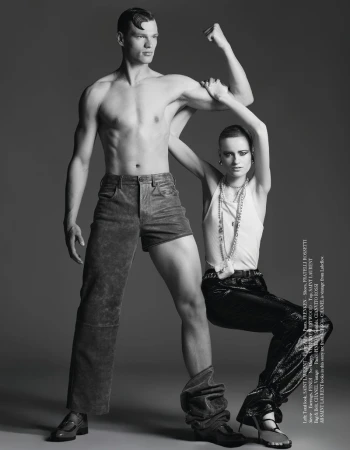 Fashion editorial shot of a shirtless man in shorts and a woman in shiny pants, posing together against a neutral backdrop.