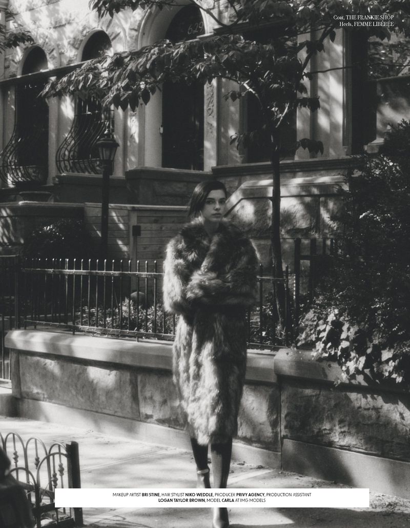 Woman in a fur coat walks on a sidewalk in front of a townhouse on a sunny day in a black and white lifestyle fashion shot.