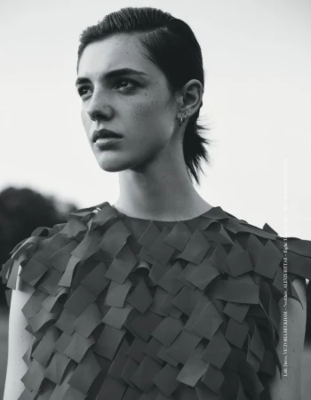 Monochrome portrait of a young woman with dark hair and eyes, wearing a patterned top, gazing into the distance against a bright sky backdrop.