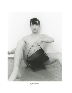 Model Anatol Modzelewski seated on a parquet floor holding a black JW Anderson handbag in a black and white editorial portrait.