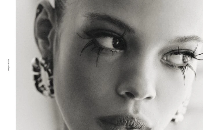 Close-up black and white portrait of a woman with dramatic eyelashes and earrings, capturing an artistic beauty aesthetic.