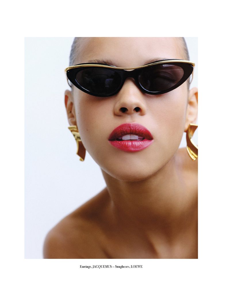 Close-up shot of a woman wearing black sunglasses and gold earrings against a white backdrop, showcasing fashion and beauty.
