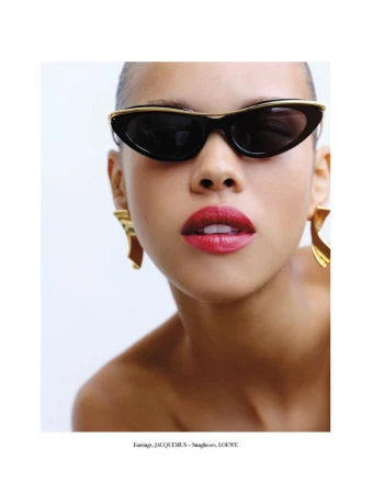 Close-up shot of a woman wearing black sunglasses and gold earrings against a white backdrop, showcasing fashion and beauty.