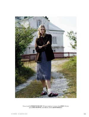 Model Femke Bloem posing outdoors in a brown jacket and blue textured midi skirt in front of a rustic estate building.