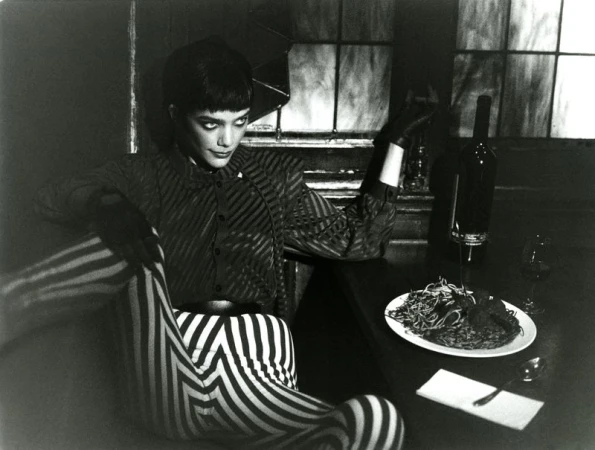Monochrome portrait of a woman in striped clothing seated at a table with wine and spaghetti, creating an editorial fashion image.