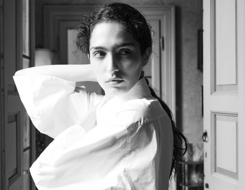 Black and white portrait of a woman in a white shirt looking away from the camera in an indoor setting with doors in the background.