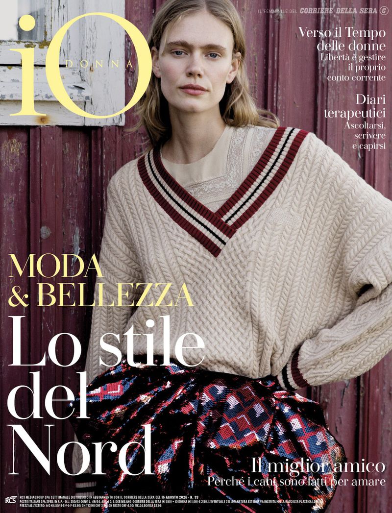 Fashion magazine cover featuring a blonde woman wearing a cable-knit V-neck sweater and a sequined skirt against a rustic wood wall.
