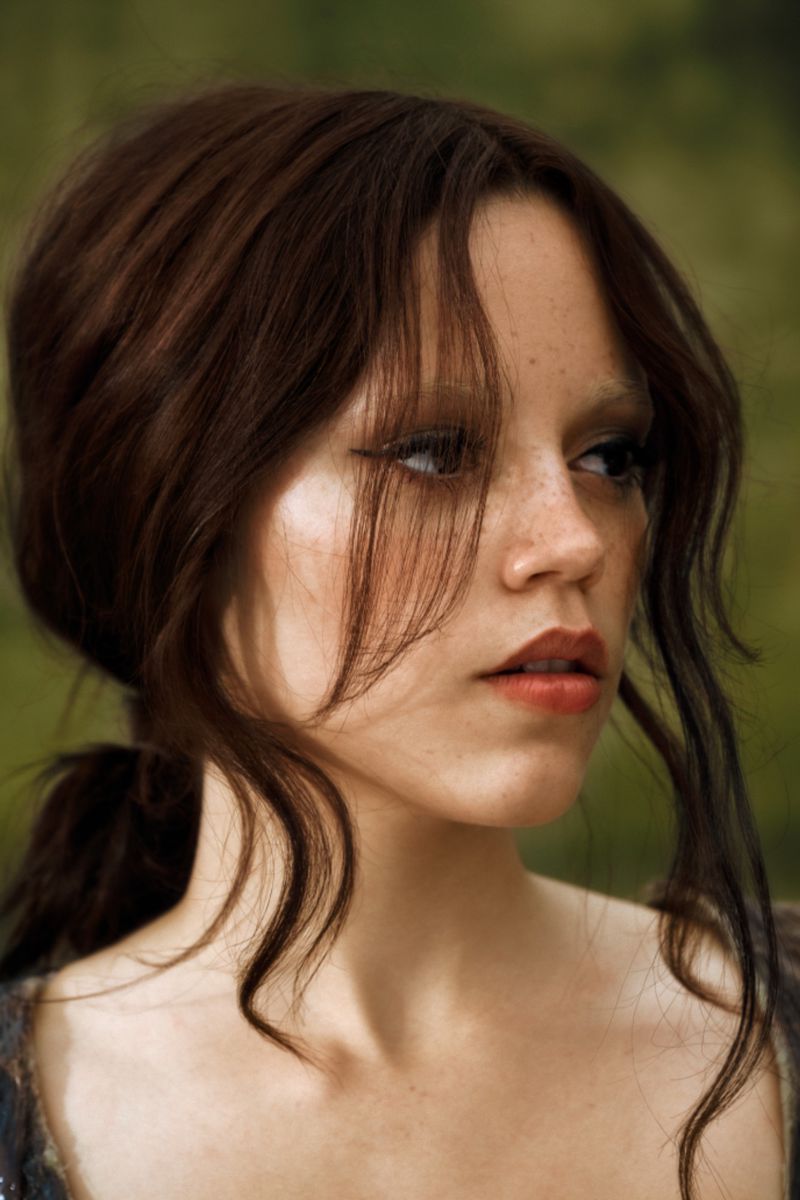Portrait of a brunette woman with freckles, wearing makeup, and looking away from the camera against a blurred green background.