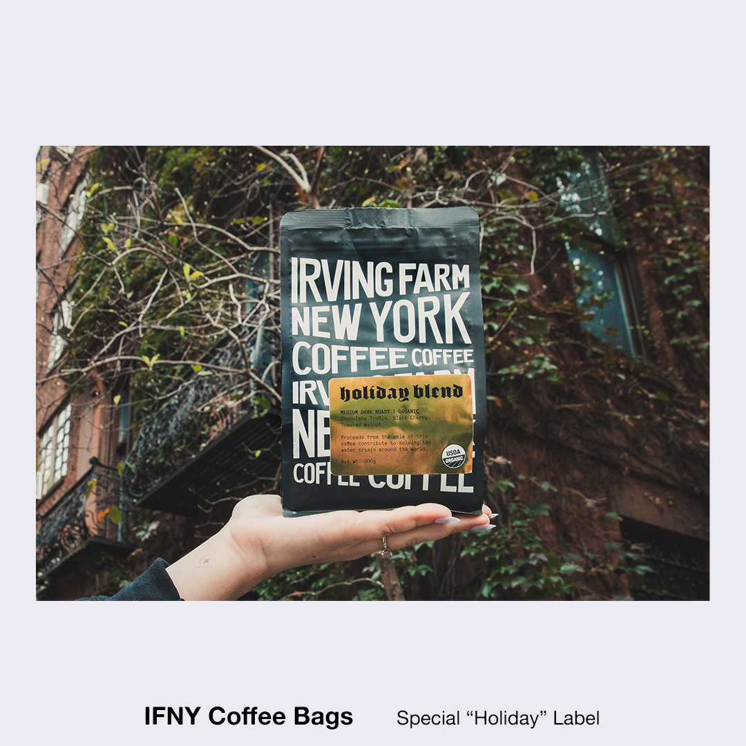 Hand holds Irving Farm New York coffee bag against a building with ivy. The bag is black with white text and a gold holiday blend label.