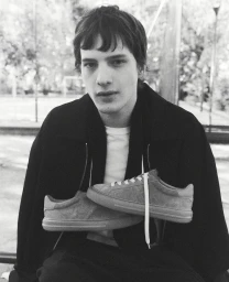 Monochrome portrait of a young male model holding suede sneakers in front of him outdoors