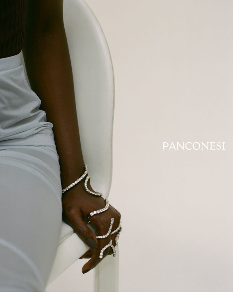 Close-up of a dark-skinned adult female's hand and arm adorned with crystal jewelry, accessorizing a light-colored dress.