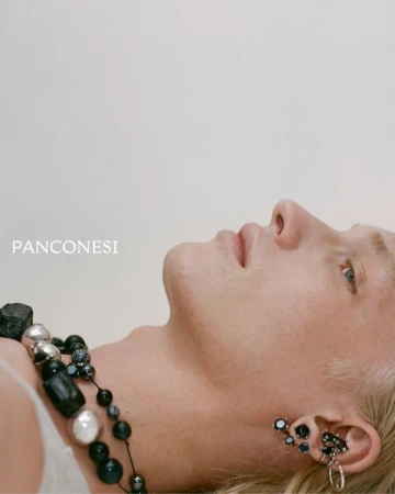 Close-up studio shot of a light-skinned person with blond hair wearing black and silver statement jewelry and designer earrings.
