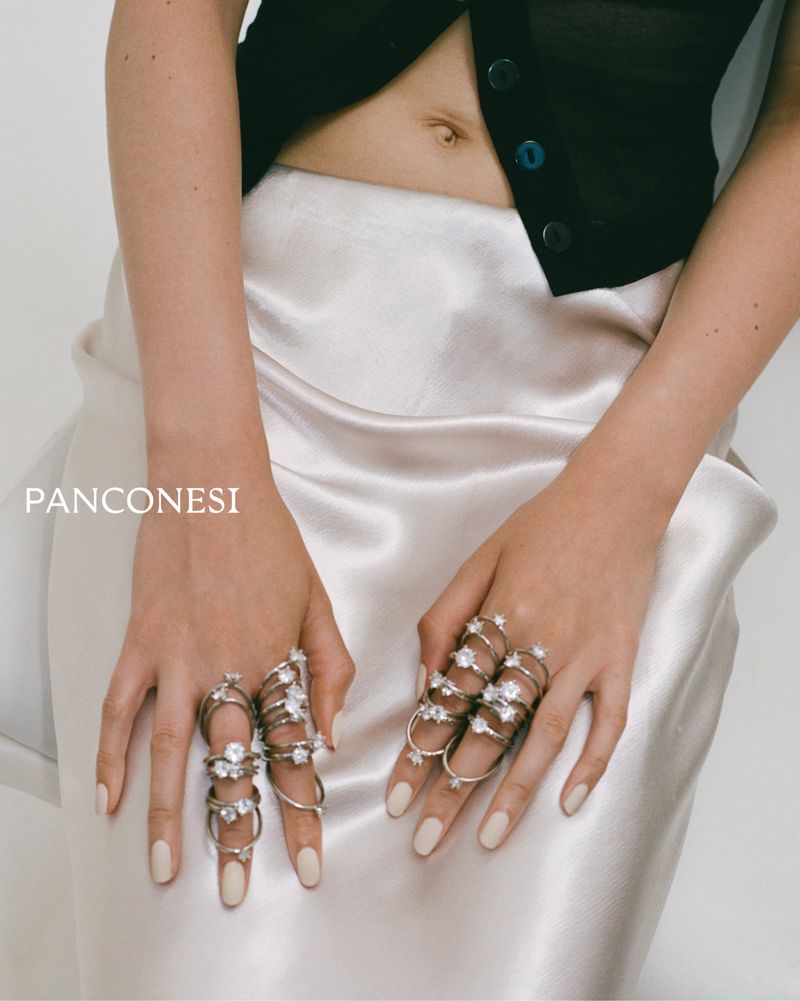 Close-up shot of a person's torso with two hands adorned with rings featuring gemstones, complemented by a satin skirt and a black top.
