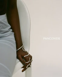 Close-up of a model's hand adorned with a coiling diamond wrap ring and bracelet, seated on a white chair against a pale studio backdrop.