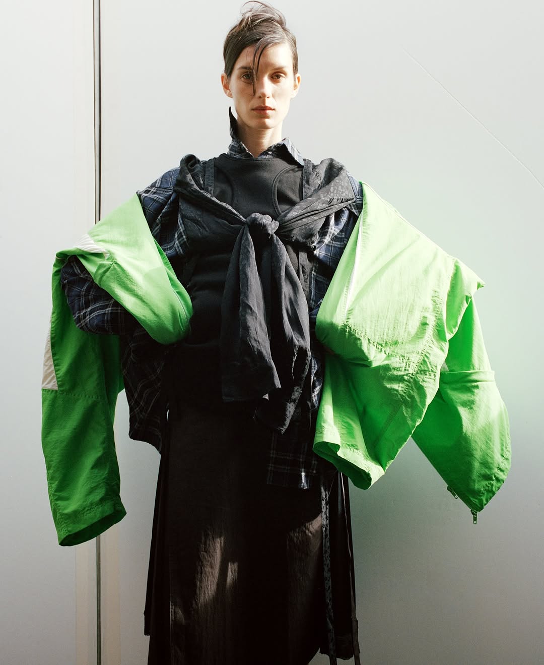 Fashion shot of a slender woman in a black top and flowing skirt. She is draped with a denim shirt and a neon green jacket.
