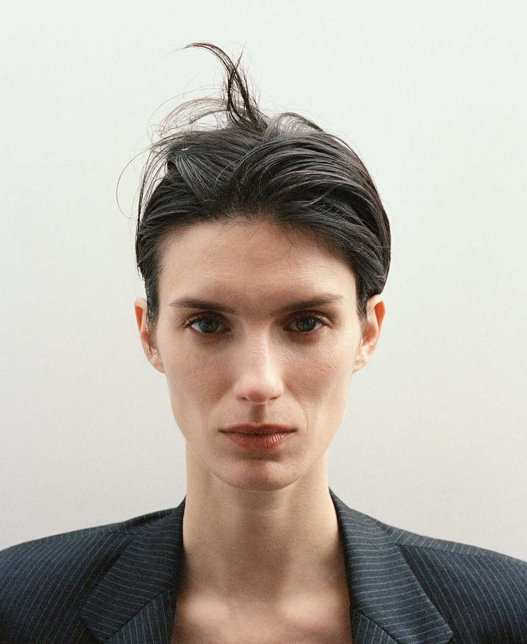 Close-up portrait of a woman with dark hair and a pinstripe blazer against a neutral light background.