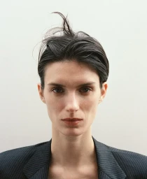 Close-up portrait of a woman with dark hair and a pinstripe blazer against a neutral light background.