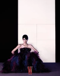 Model seated wearing a dark feathered dress against a minimalist panel wall for W Magazine China by Zeng Wu