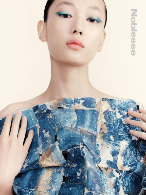 Asian model wears blue graphic top and matching eye makeup in a close-up studio shot for a fashion editorial in diffused lighting.