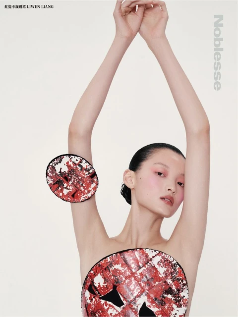 Editorial fashion shot of a bare-chested Asian model with arms raised wearing round red-and-white avant-garde discs against a white backdrop.