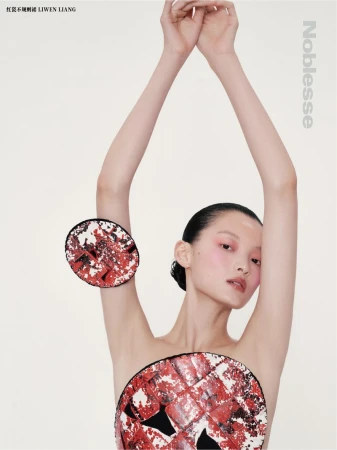 Editorial fashion shot of a bare-chested Asian model with arms raised wearing round red-and-white avant-garde discs against a white backdrop.