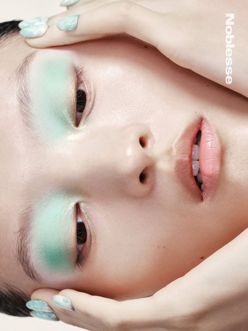 Portrait of a woman with mint eyeshadow and nail polish, fair skin, and hands framing her face, viewed from a high angle.