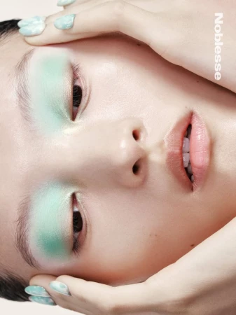 Portrait of a woman with mint eyeshadow and nail polish, fair skin, and hands framing her face, viewed from a high angle.