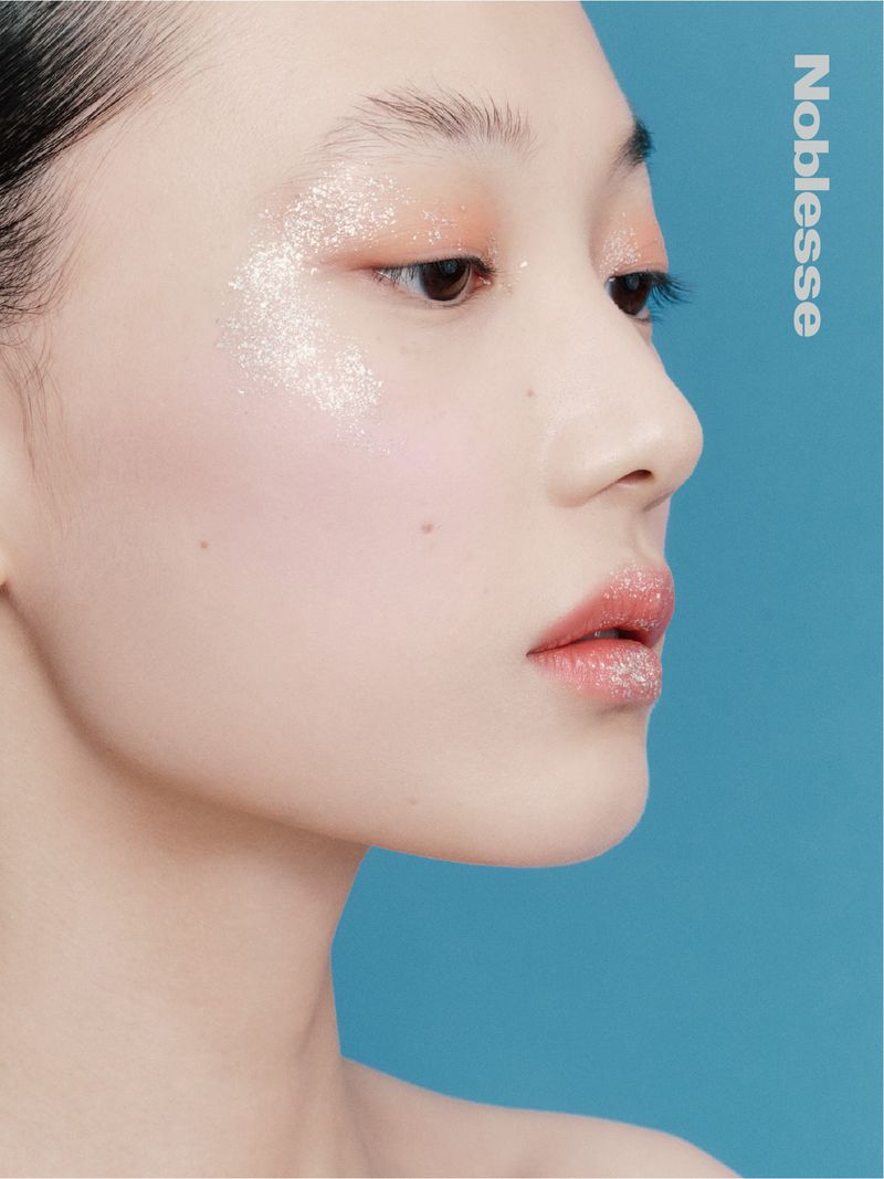 Close-up portrait profile of a model with glitter makeup on her eyes and lips against a solid blue background