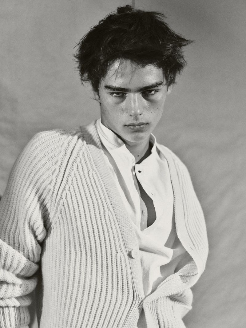 Black and white portrait of a young adult male wearing a white button-down shirt and cardigan in a photo studio setting.