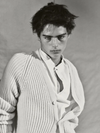 Black and white portrait of a young adult male wearing a white button-down shirt and cardigan in a photo studio setting. 