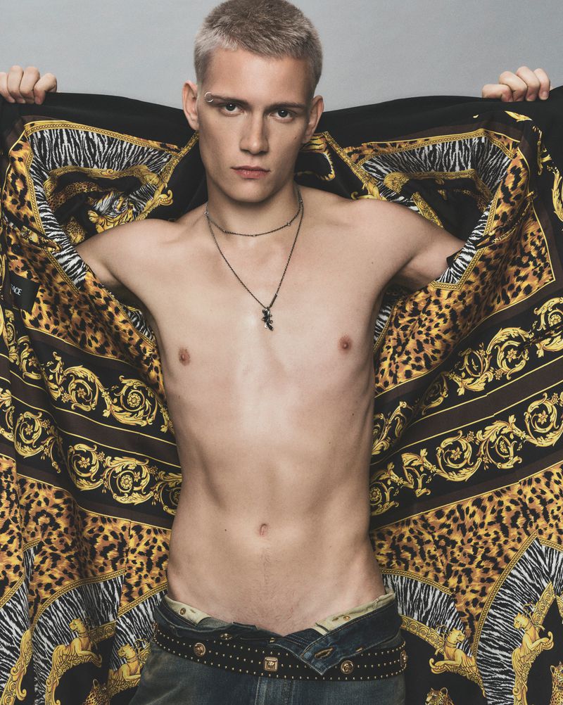 Young adult man poses with a designer shawl featuring animal and baroque patterns, showcasing his toned physique and accessorized look.