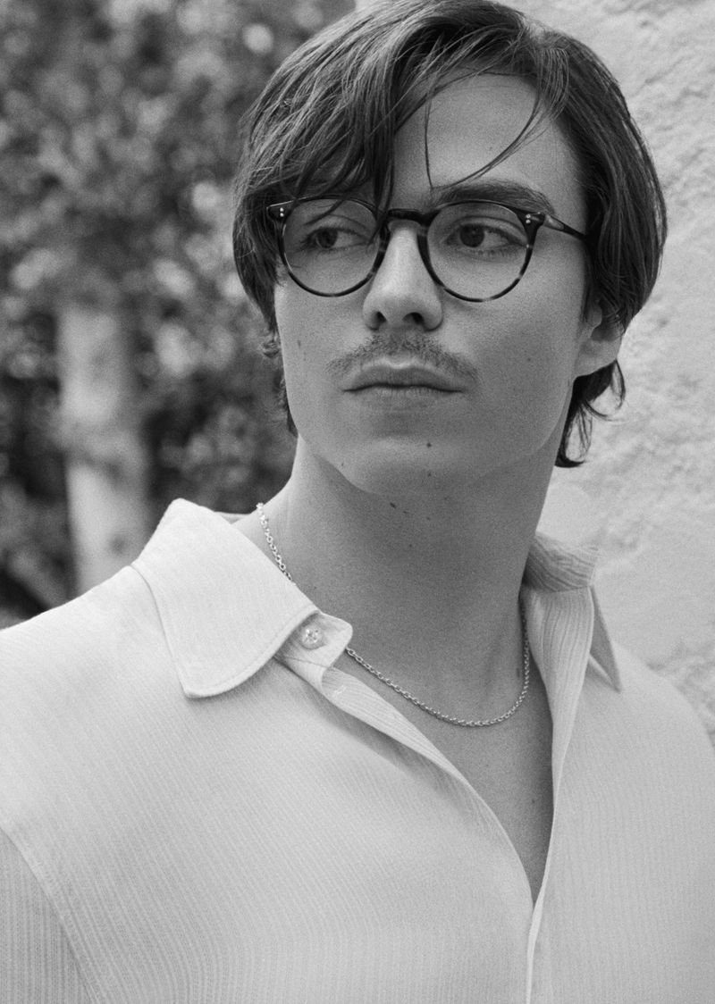 Black and white portrait of a young man wearing glasses and a collared shirt, looking off to the side with a neutral expression.