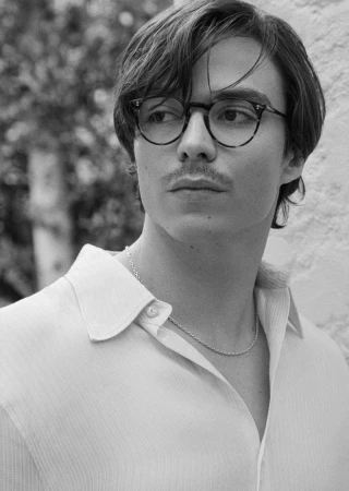 Black and white portrait of a young man wearing glasses and a collared shirt, looking off to the side with a neutral expression.