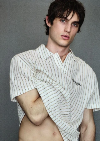 Close-up portrait of a fair-skinned adult male with dark hair wearing a striped button-down shirt against a grey backdrop in a photo studio.