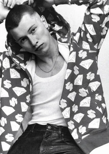 Close-up portrait of a male model wearing a patterned zip-up hoodie over a white tank top against a white backdrop.