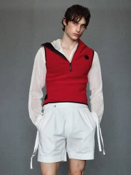 Male model in red vest over white mesh long-sleeve top and white shorts against a textured grey background.