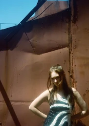 Model Lola Tung in a black and white patterned dress standing against a rusty industrial metal wall outdoors.