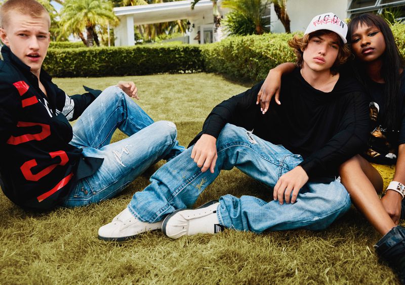 Three young adults sit on a grassy lawn with palm trees and a modern house in the background, wearing contemporary casual fashion.