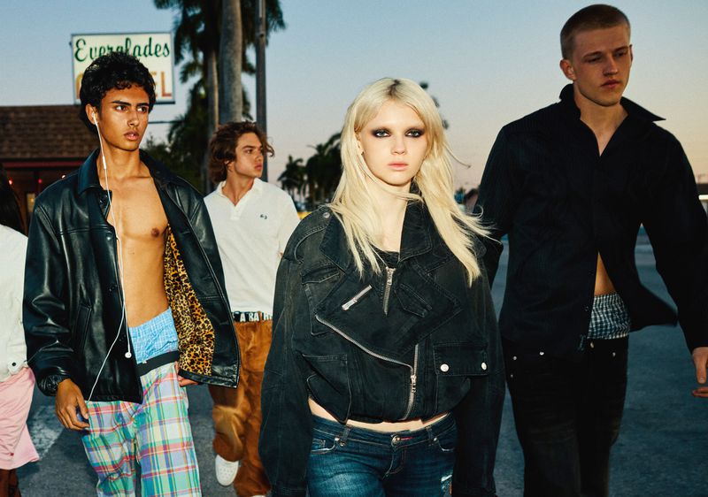 Four young adults walk outside near a building. The group features diverse fashion styles, posing for a fashion editorial style photo.