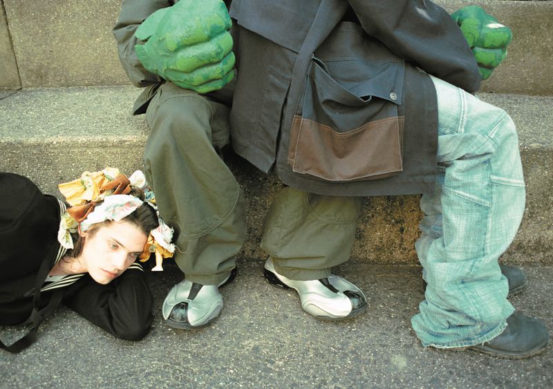 Two people, one wearing green Hulk-like gloves and light blue jeans, the other lying on the ground wearing a sailor outfit and headscarf.
