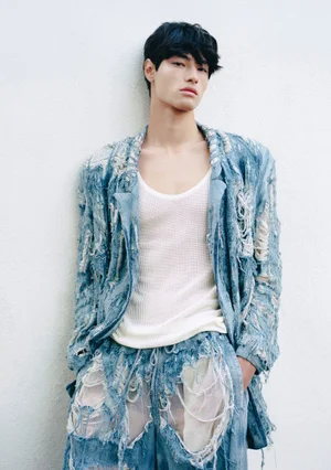 Model wearing a distressed light blue denim jacket and matching trousers against a plain white wall.