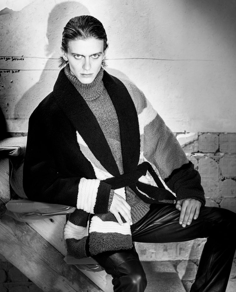Monochrome portrait of an adult male fashion model with wet hair, wearing a gray turtleneck sweater and a striped robe, looking at the camera.