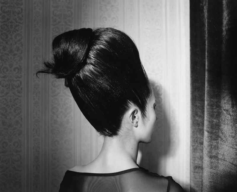 Black and white portrait shot of an adult female with a dramatic updo hairstyle facing away from the camera in an indoor setting.