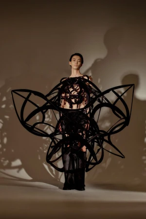 Model Gendai Funato wearing a large black sculptural wearable frame for the Ryunosukeokazaki S/S 26 lookbook in a lit studio.