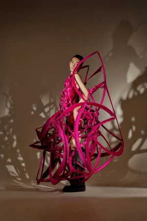 Model Gendai Funato wearing a sculptural magenta ribbon cage dress by Ryunosuke Okazaki casting dramatic shadows in a studio setting.