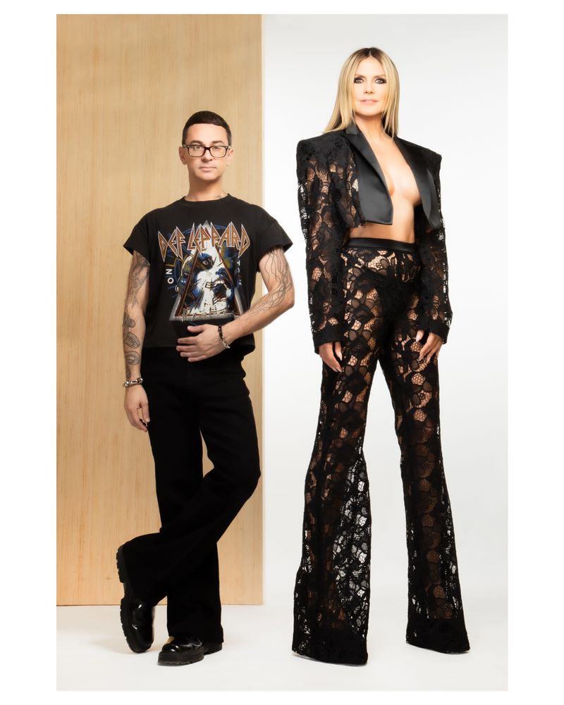 Fashion shot of Heidi Klum in a lace outfit with a designer in a band T-shirt, against a neutral backdrop, studio lighting.