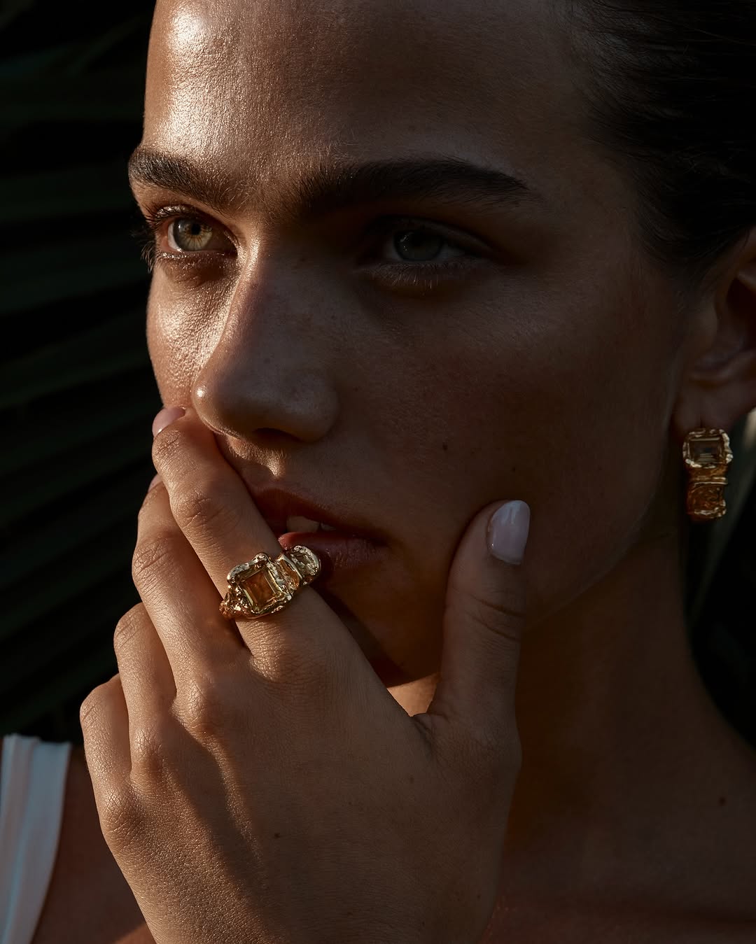 Close-up of a model wearing a large statement ring and earrings, emphasizing jewelry design against a blurred nature background.